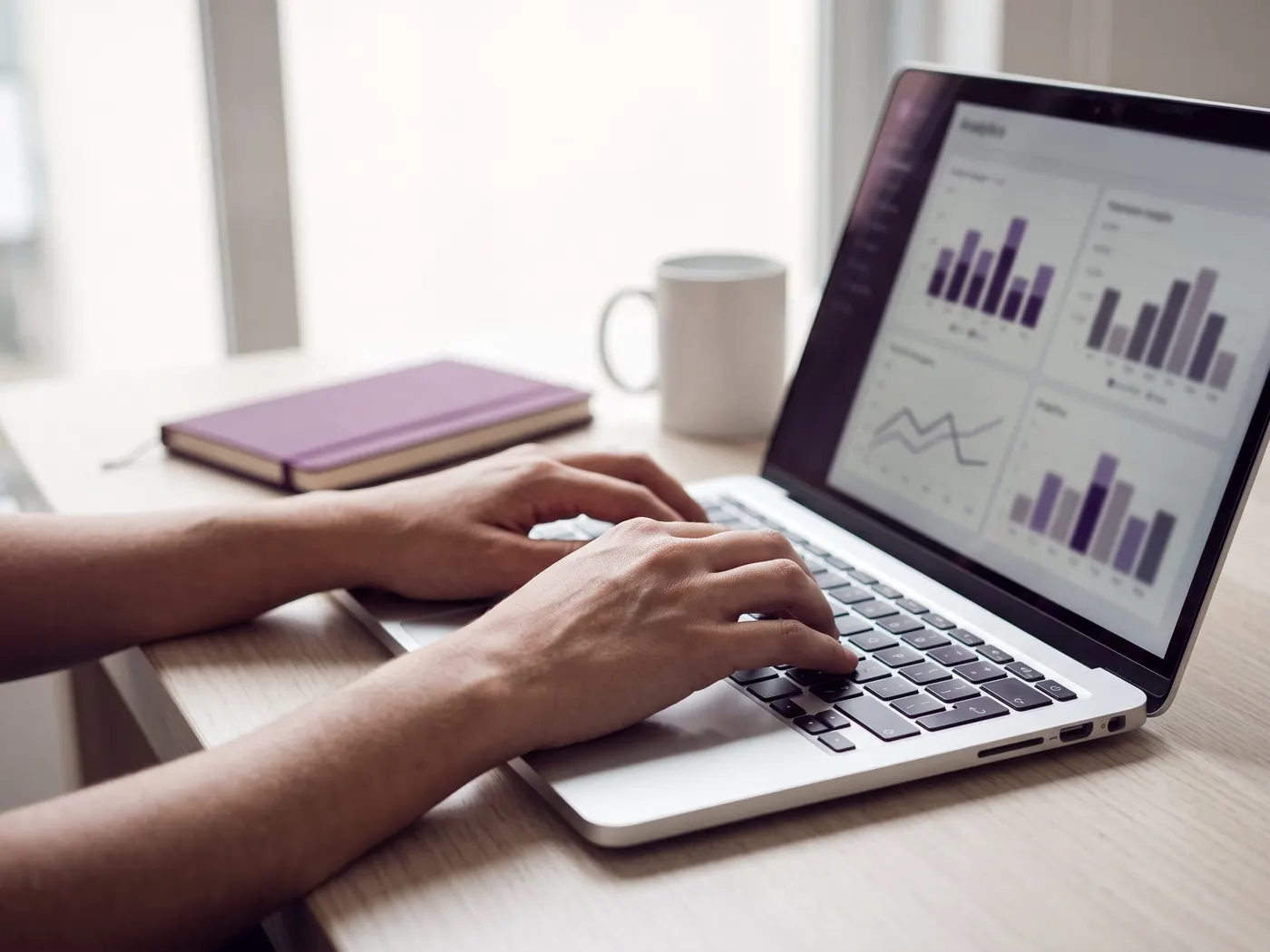 Mãos digitando em um notebook que mostra gráficos de barras e de linha em tons de roxo